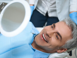 homem de meia idade sorrindo em frente ao espelho e ao lado do dentista